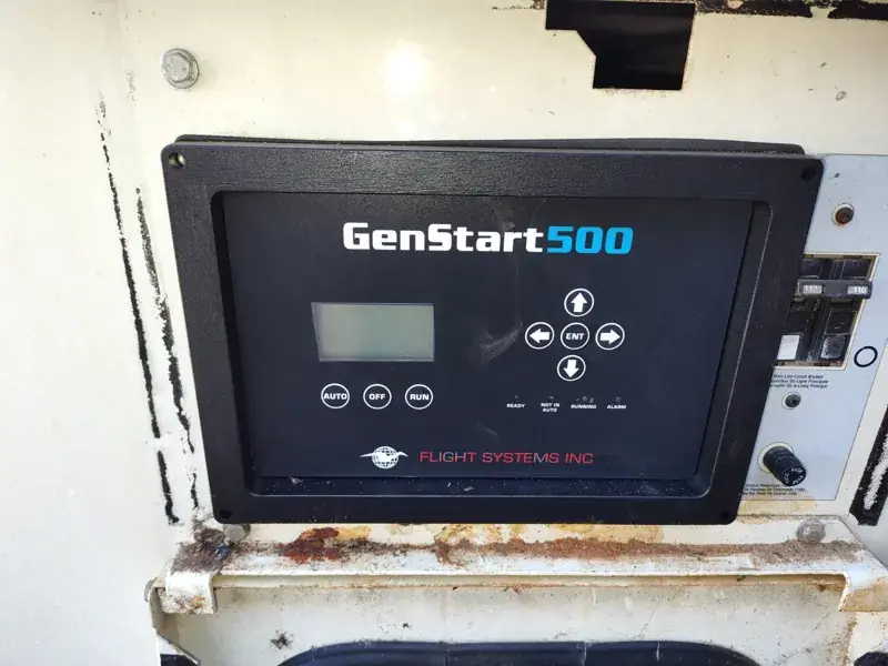 GenStart 500 controller by Flight Systems Inc. with a small display, arrow keys, Auto, Off and Run buttons and status lights, set in a weathered cream panel beside a circuit breaker.
